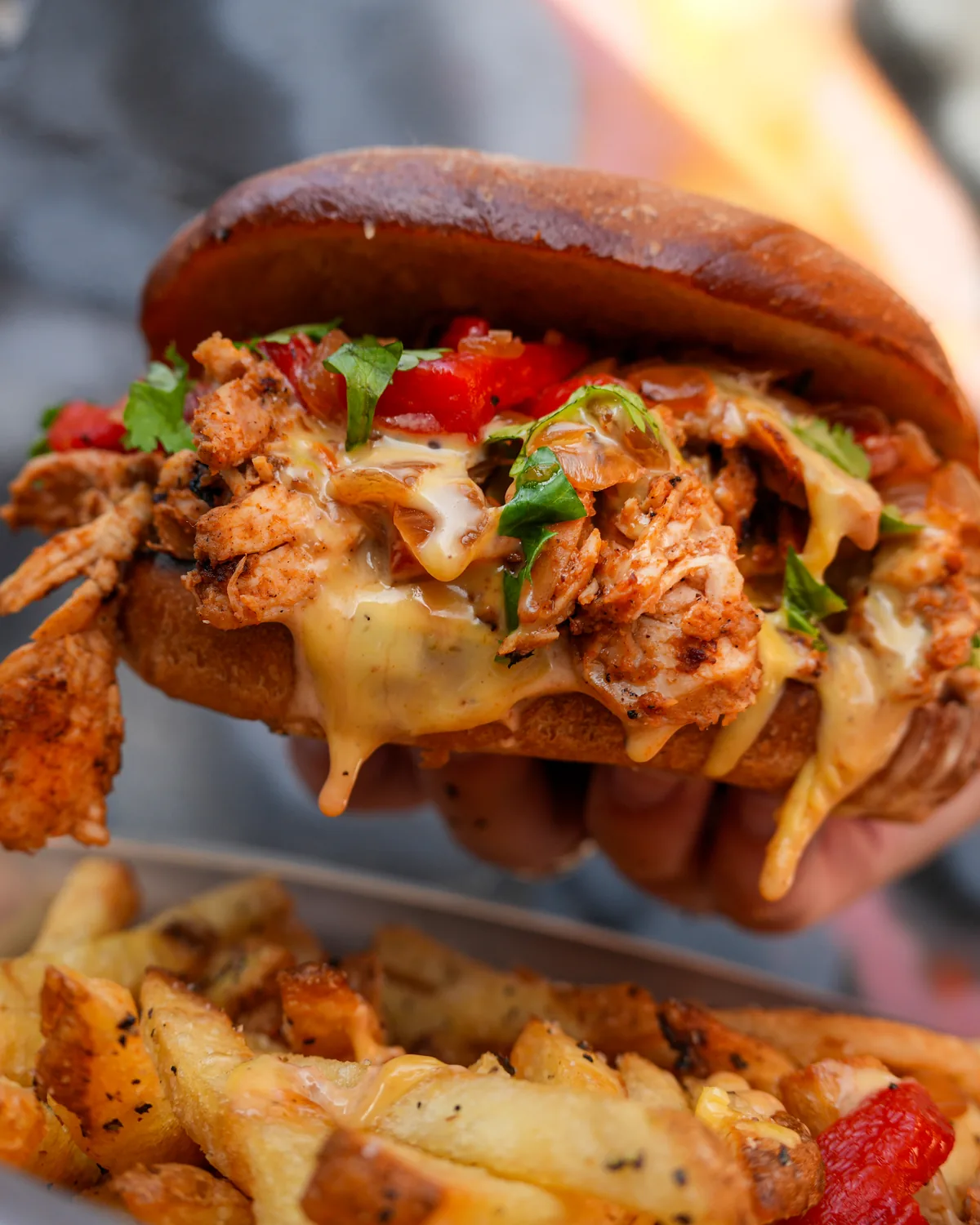 Smoked Chicken Hatch Chile Cheesesteak, pulled smoked chicken with Hatch chile queso, roasted red peppers and cilantro on a telera roll, held over fries
