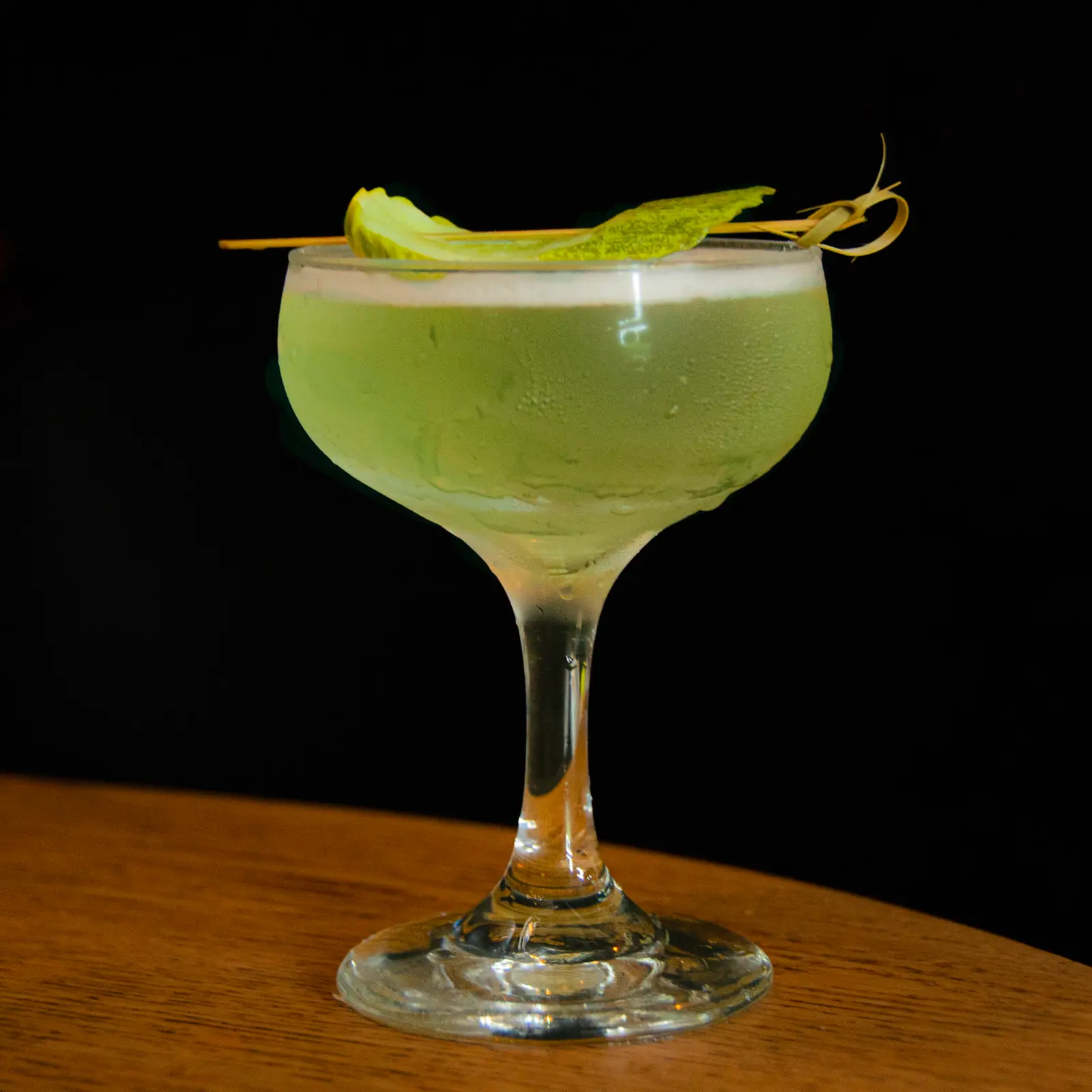 The Pickle Martini in a coupe with a skewered pickle chip