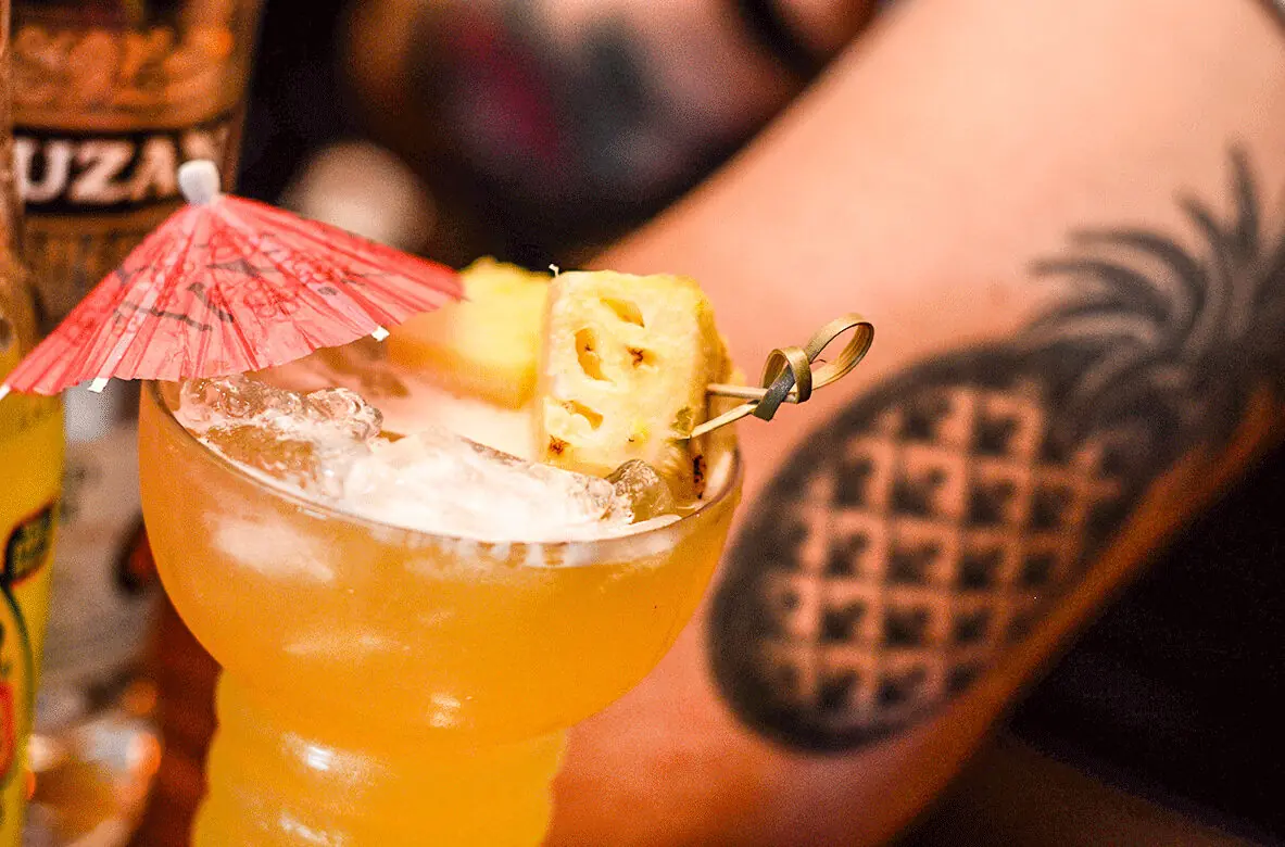 The Pineapple Creamy Marg — coupe, fresh pineapple, umbrella, and a matching tattoo