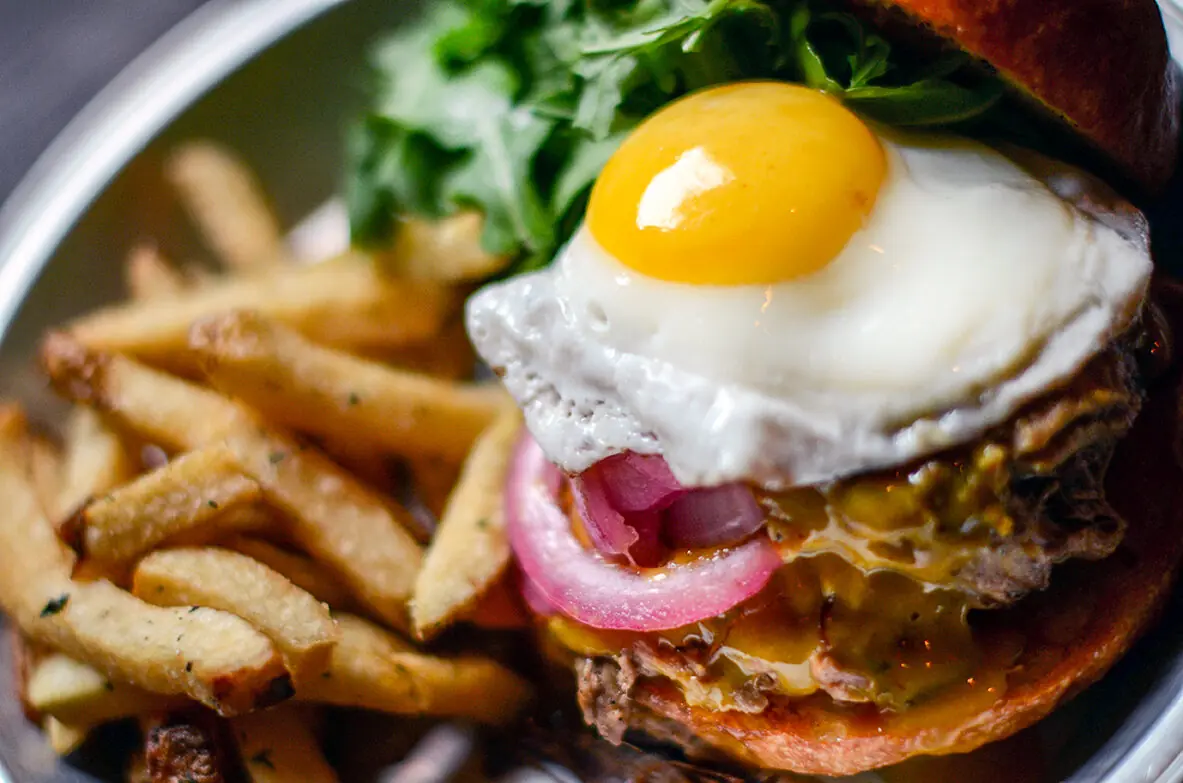 NSYC burger topped with a sunny-side-up egg, pickled red onion and arugula, with hand-cut fries